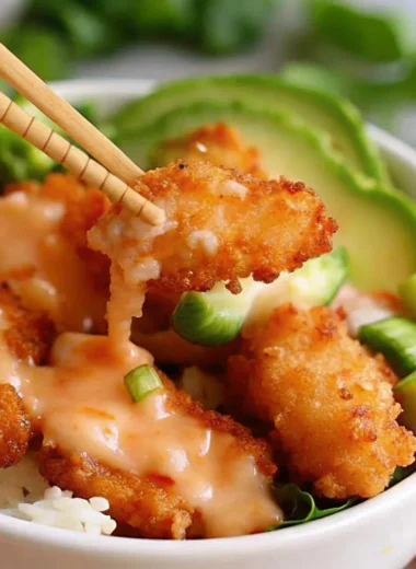 Crispy Bang Bang shrimp served over white rice with spicy mayo, avocado slices, cucumber, and green onions in a bowl.