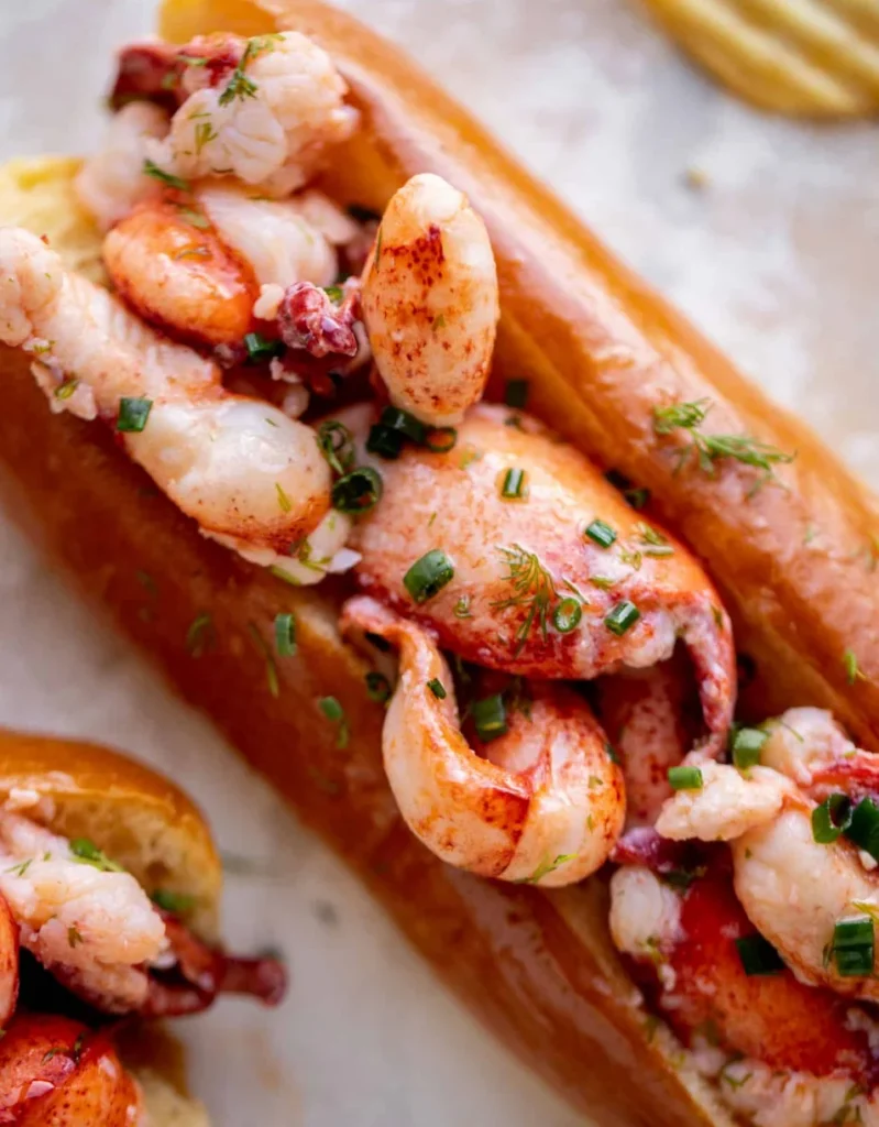 Warm buttery lobster roll filled with succulent lobster meat and garnished with fresh herbs in a toasted bun.