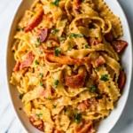 Creamy tomato and lobster pasta garnished with parsley, served on a white oval plate.