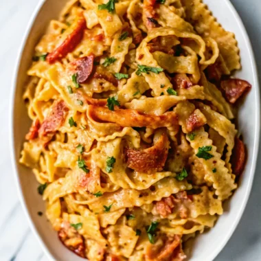 Creamy tomato and lobster pasta garnished with parsley, served on a white oval plate.