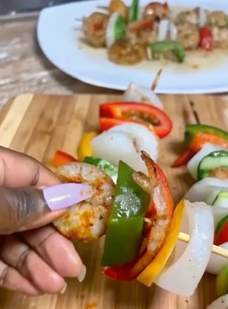 Grilled shrimp kabobs with bell peppers, onions, and a side of seasoned pasta on a white plate.