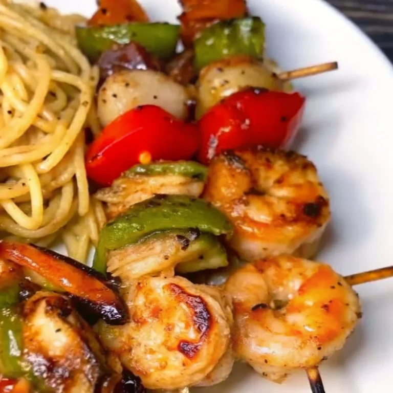 Grilled shrimp kabobs with bell peppers, onions, and a side of seasoned pasta on a white plate.
