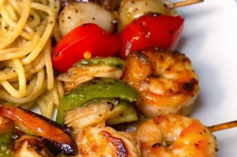Grilled shrimp kabobs with bell peppers, onions, and a side of seasoned pasta on a white plate.
