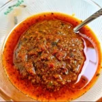 Rich and spicy Lotus Seafood Sauce served in a glass bowl with a spoon, showcasing its vibrant red oil layer and chunky texture.