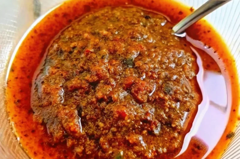 Rich and spicy Lotus Seafood Sauce served in a glass bowl with a spoon, showcasing its vibrant red oil layer and chunky texture.