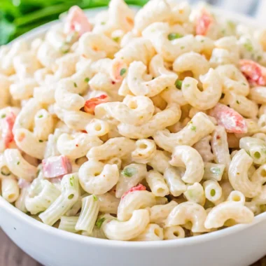 A close-up of a creamy macaroni salad with shrimp, featuring elbow macaroni, diced celery, red bell pepper, and a rich mayonnaise-based dressing, served in a white bowl.