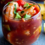 Colorful Mexican shrimp cocktail served in a glass with tomato sauce, avocado chunks, fresh cilantro, and plump shrimp.