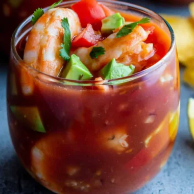 Colorful Mexican shrimp cocktail served in a glass with tomato sauce, avocado chunks, fresh cilantro, and plump shrimp.