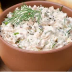 Creamy salmon spread with fresh dill garnish served in terracotta bowl alongside crackers