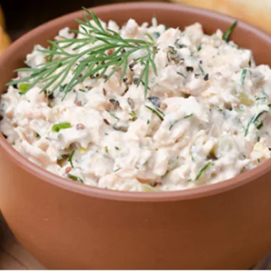 Creamy salmon spread with fresh dill garnish served in terracotta bowl alongside crackers