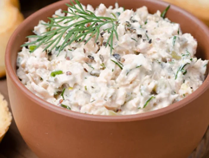 Creamy salmon spread with fresh dill garnish served in terracotta bowl alongside crackers