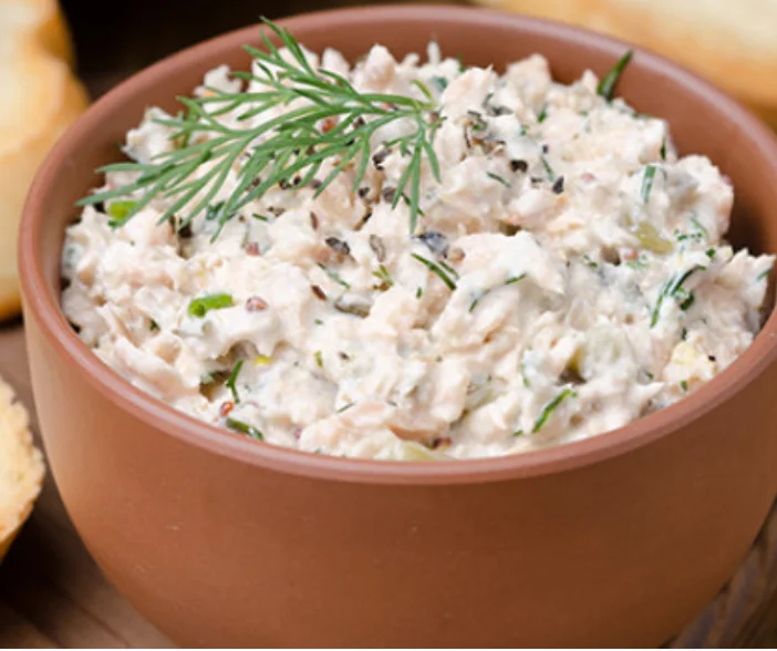 Creamy salmon spread with fresh dill garnish served in terracotta bowl alongside crackers