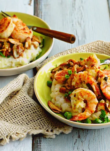 Two bowls of shrimp and grits topped with bacon, mushrooms, and green onions on a rustic wooden table.