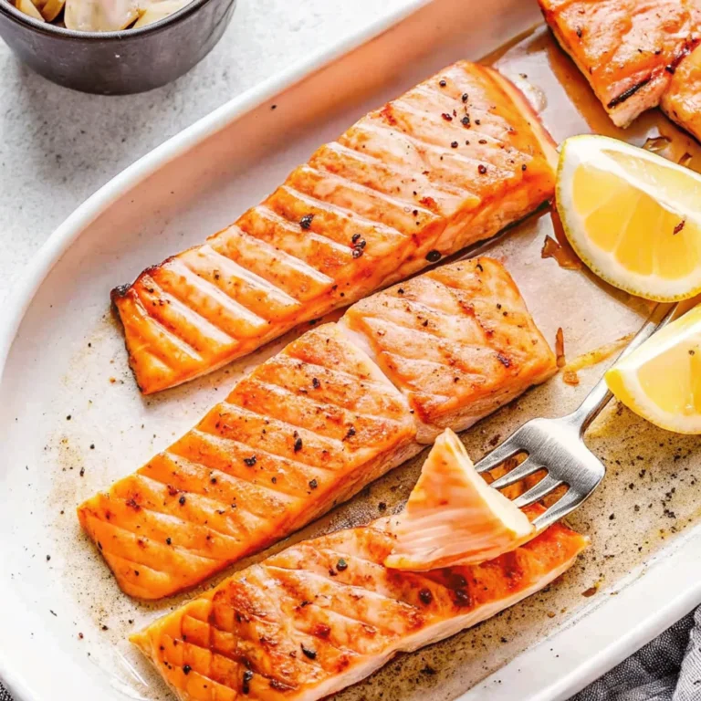 Grilled Coho salmon fillets on a white serving plate with lemon wedges and black pepper seasoning.
