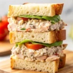 Close-up of a stacked tuna sandwich made with sourdough bread, fresh spinach, tomato slices, cucumber, and creamy tuna filling.